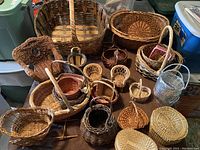 Overview of assortment of different sizes and shapes of wicker and woven baskets arranged together on floor.
