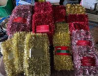 Multiple packaged strands of red, gold, and pink-silver tinsel garlands arranged on a surface.