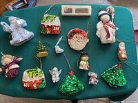Assorted Christmas tree ornaments including cloth angels, fabric and resin houses, sequin Christmas trees, resin snowman, Santa face, small mouse figure, small stocking, and fabric doll.