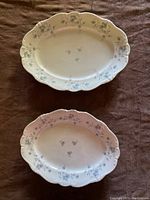 Top view of two white porcelain oval platters with blue floral garland pattern on scalloped edges.