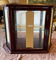 Front view of mini curio cabinet showing wooden frame, glass front door with a keyhole and a shelf inside.