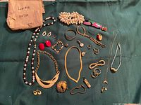 Full layout of assorted vintage women's jewelry including necklaces, bracelets, rings, earrings, brooches, and pendants displayed on dark green cloth.