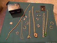 Full assortment of jewelry laid out on green cloth showing necklaces, earrings, brooches, and jewelry box