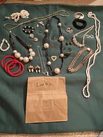 Full lot with assorted women's jewelry including necklaces, bracelets, earrings, rings, and pendants shown on a green background.