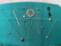 Photo showing assorted women's jewelry laid out on a green surface, including necklaces, rings, bracelets, earrings, a heart-shaped locket on black cord, and a round locket or brooch.