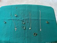 Assortment of vintage women's jewelry on green fabric, showing rings and necklaces with pendants including a cross pendant and a leaf or heart shape pendant.