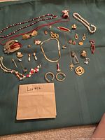 Full lot overview showing assortment of jewelry including necklaces, bracelets, brooches, earrings, rings, and pins spread on green cloth surface.