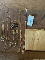 Full view of assorted women's vintage jewelry including necklaces, earrings, and a bracelet on brown fabric background