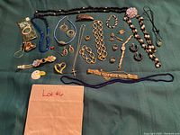 Full lot of assorted women's vintage jewelry laid out on green fabric including necklaces, bracelets, rings, earrings, brooches, pins and a watch.