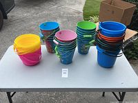 Photo of multiple kids buckets in various colors on a table showing yellow, pink, blue, green, orange buckets stacked and lined up.