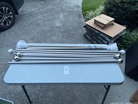Four curtain rod sets laid out on a folding table, showing the full rods with ends and extension tubes