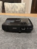 Front view of black Epson projector on table showing lens, ventilation, and HDMI label.