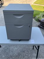 Front view of gray metal file cabinet showing two drawers, with key lock on bottom drawer and casters.