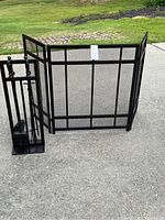 Photo of the black metal fireplace screen with three hinged panels showing grid design, placed on concrete outside.
