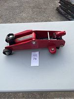 Side view of the red hydraulic car jack showing the wheels, lift arm, and main body.