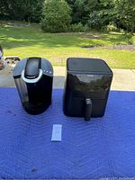 Keurig coffee maker and Cosori air fryer side by side on blue blanket outside.