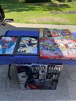 Five Marvel-themed artworks displayed outdoors on a table including 3 canvases and 2 framed pictures
