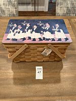 Photo of rectangular wooden picnic basket with printed lid showing waiters carrying trays.