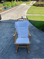 Frontal view of light wooden rocking chair showing white quilted cushion on backrest and seat with ruffled edges.