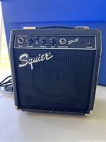 Front view of the Squier amplifier showing input jack, volume, treble, bass knobs, headphone jack, power switch, and Squier logo.