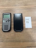 TI-89 Titanium calculator and black protective cover laid out side by side on wooden surface.