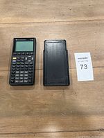 TI-85 calculator with protective cover placed on a wood surface for overall lot view.