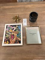 Photo shows a wooden surface displaying two picture frames: one white bordered with colorful tiger artwork, one brass bordered terrace floating frame. Also shown is a glossy dark gray ceramic pot with white base and a brass floral decorative accessory.