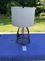 Full view of the table lamp showing its open wire mesh base and white cylindrical lampshade.