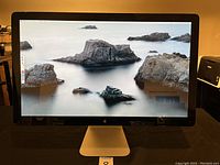 Front view of the 27-inch Apple Thunderbolt display showing screen turned on with rocky sea wallpaper.