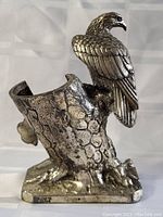 Front and side view of silver plated eagle perched on textured tree stump base, showing detailed feathers and hollow angled holder compartment.