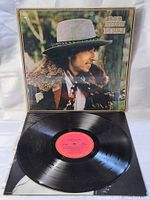 Vinyl record and open inner sleeve visible. Vinyl label visible as red Columbia label. Cover shows Bob Dylan in profile with fur collar and hat