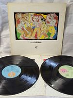 Two black vinyl LP records displayed with colored labels, blue and green, and original cardboard album cover with colorful front artwork featuring stylized human figures.