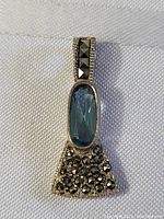 Front view of a sterling silver Art Deco style pendant featuring a vertically set aqua marine gemstone with marcasite stones on the bail and trapezoidal lower section.