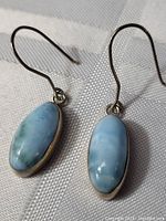 Close-up view of both sterling silver earrings with baby blue oval stones laid on white textured fabric.