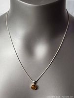 Long view of sterling silver necklace displayed on a mannequin bust featuring the small round amber pendant.