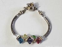 Full view of sterling silver bracelet with textured and patterned silver tube segments and multicolored jewels.
