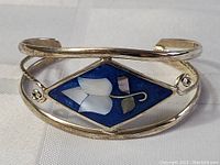 Close-up of sterling silver bracelet with diamond-shaped blue enamel and mother of pearl floral inlay design.