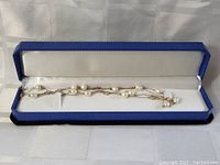 Pearl necklace coiled in jewelry box with white cushioned interior.