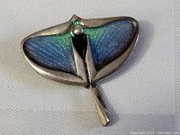 Front view of vintage sterling silver stingray pin brooch pendant showing blue and green enamel wings and silver body.