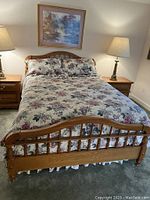 Front view of queen size bed with oak finish and floral bedding, showing headboard and one nightstand with lamp.