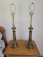 Pair of two brass column lamps shown without shades, revealing bulb and socket details. Lamps have tiered bases and decorative vertical sections on columns.