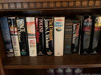 Photo showing 11 hardcover books by James A. Michener arranged on a wooden shelf. Titles visible include 'The Source,' 'Space,' 'Mexico,' 'Poland,' 'The Covenant,' 'Caribbean,' 'Texas,' and 'Alaska.' Books appear in excellent condition with intact dust jackets.