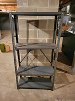 Black metal bookshelf with three shelves, showing signs of wear and light rust, empty without items on shelves.