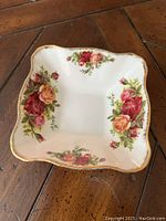 Square bone china dish with floral rose design and gold trim on scalloped edges, top view