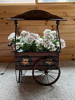 Front view of rustic wooden flower cart filled with artificial flowers showing floral painted details and large metal wheels