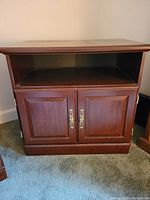 Front view of the small wooden cabinet showing paneled double doors with brass handles and an open top shelf.
