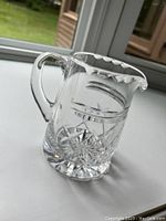 Clear crystal pitcher with decorative floral and starburst cuts, scalloped spout and handle.