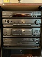 Four Sony audio components stacked vertically inside a wooden cabinet shelf: AM/FM tuner, graphic equalizer, double cassette player, and 5-disc CD changer with full front panel buttons and digital displays.