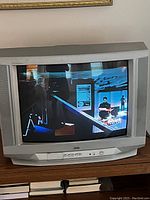Front view of the JVC CRT TV powered on and displaying an image on the screen, showing the silver-grey plastic frame and front buttons.