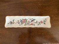 Top view of rectangular porcelain trinket dish showing floral pattern with pink, blue, green flowers and gold leaf rim